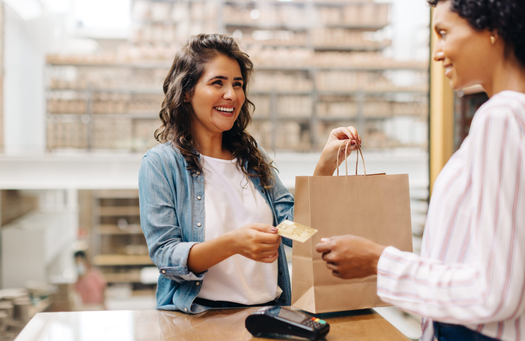 Customer making a credit card payment while holding a shopping bag at a retail store counter.