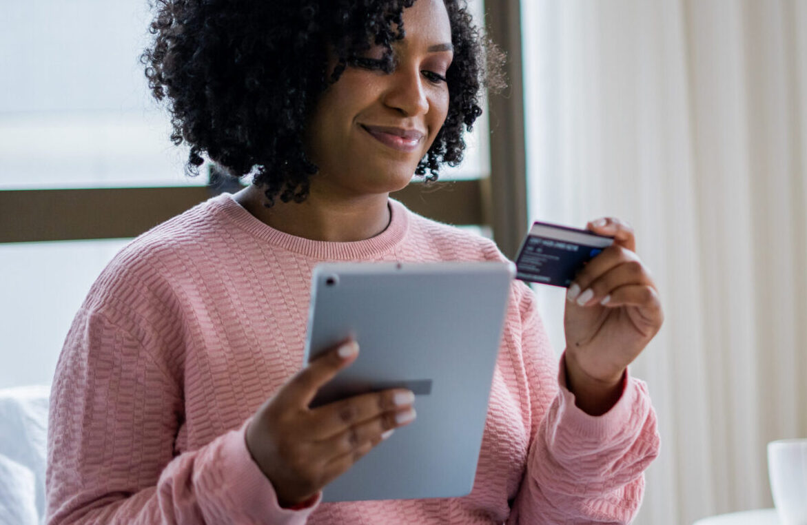 Woman holding a credit card and using a tablet for an online payment.