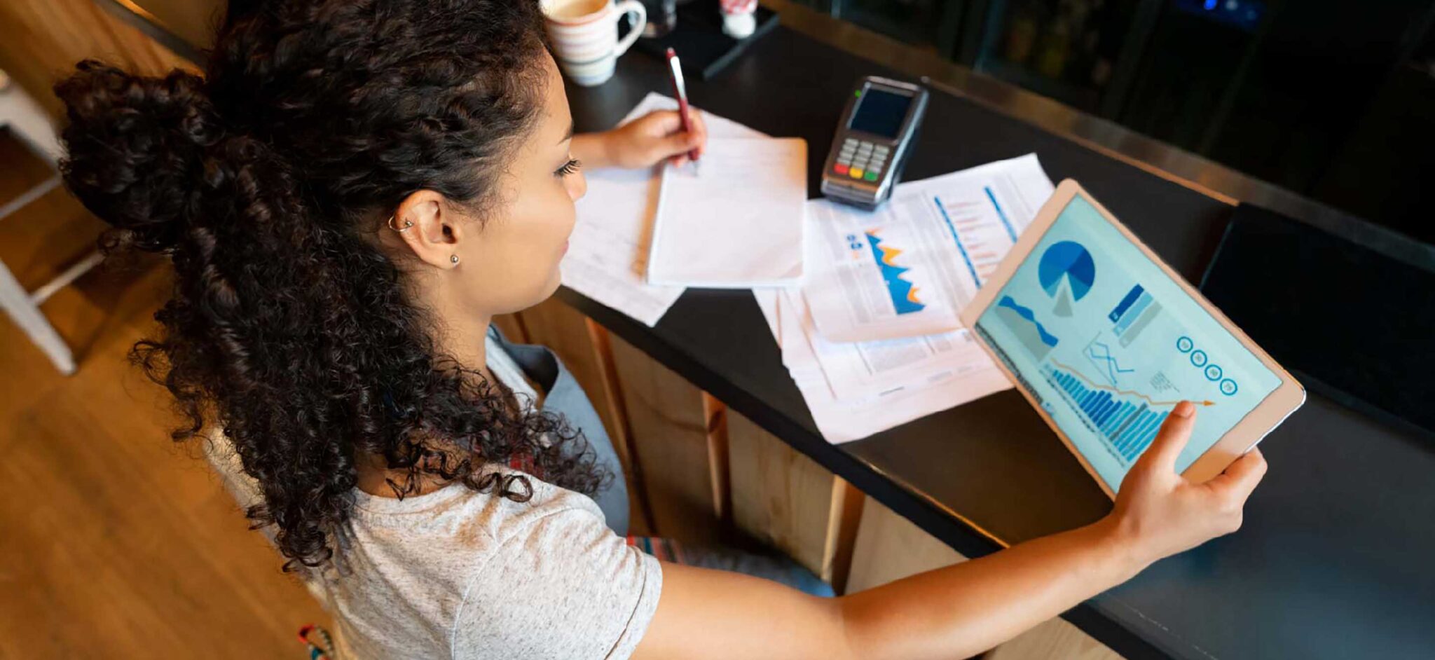 Woman reviewing financial data on a tablet with documents on the table.