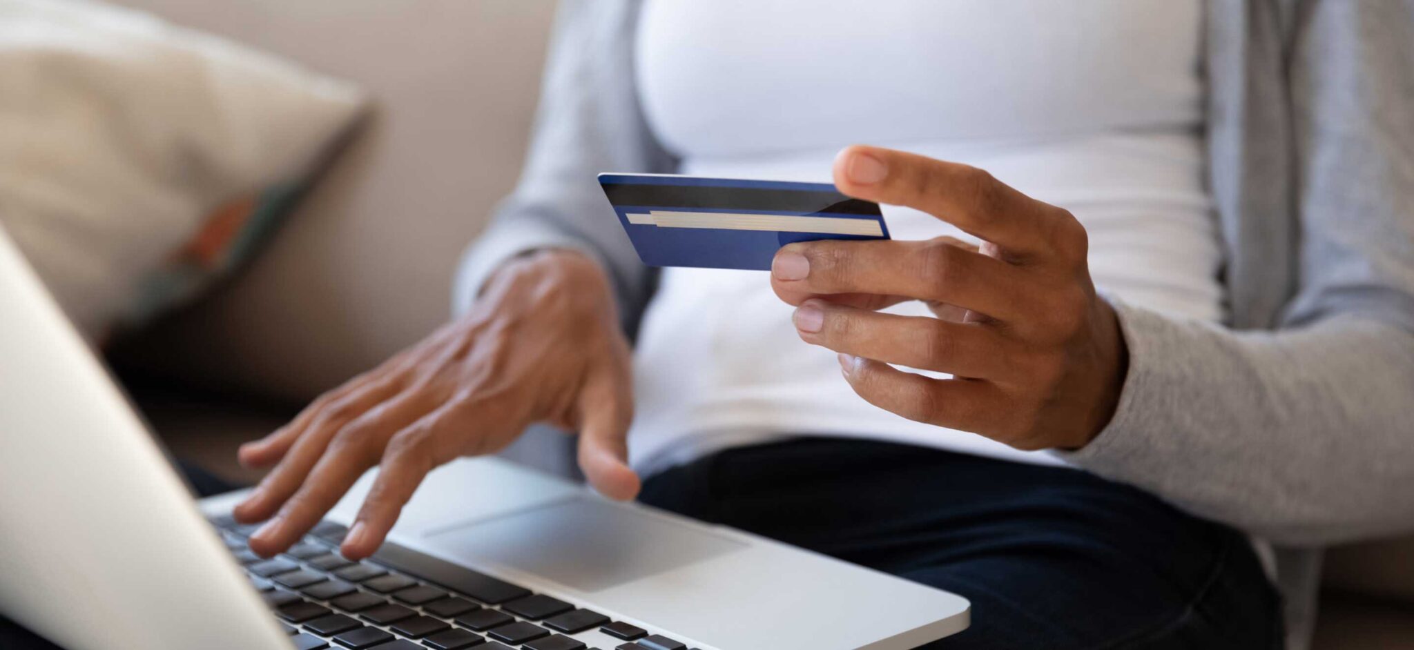 Person holding a credit card while typing on a laptop for an online payment.