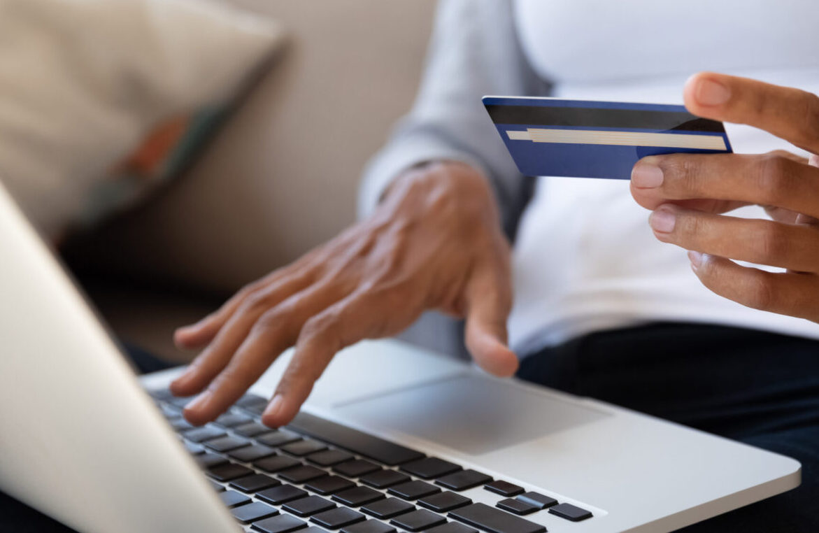 Person holding a credit card while typing on a laptop for an online payment.