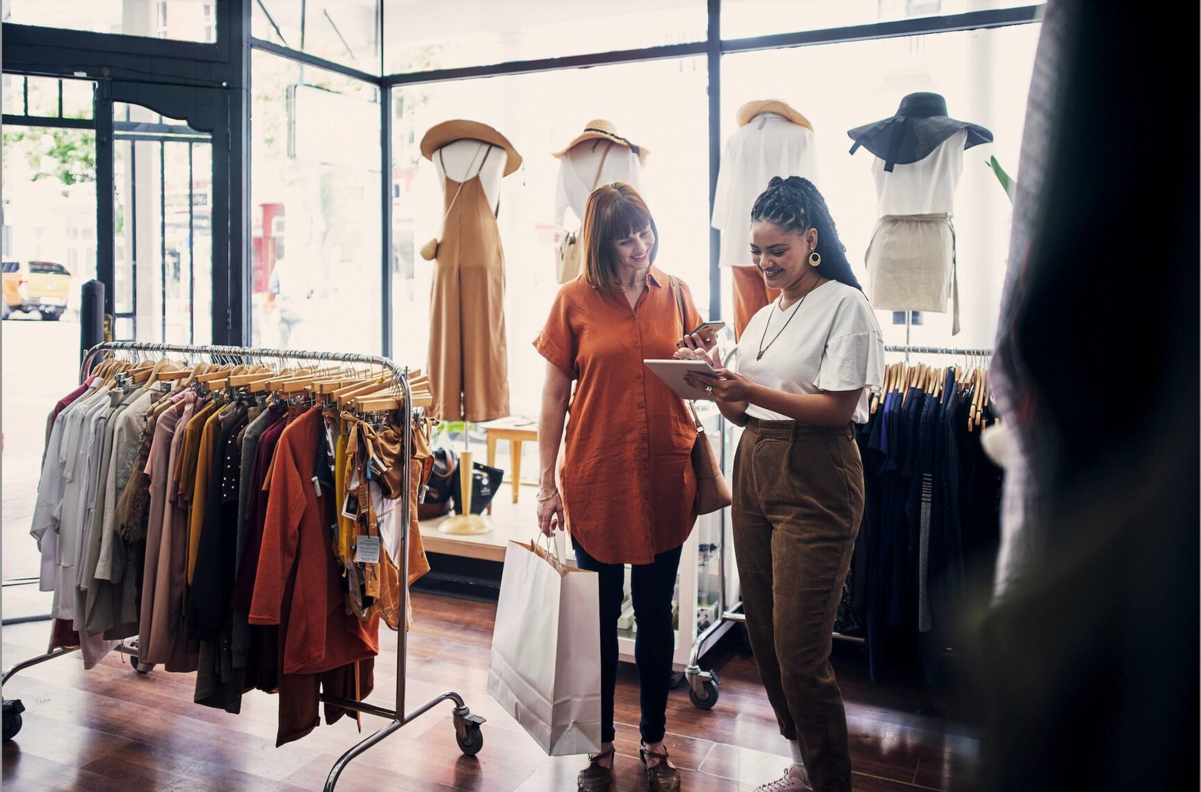 Two women discussing items in a clothing store, one holding a tablet.