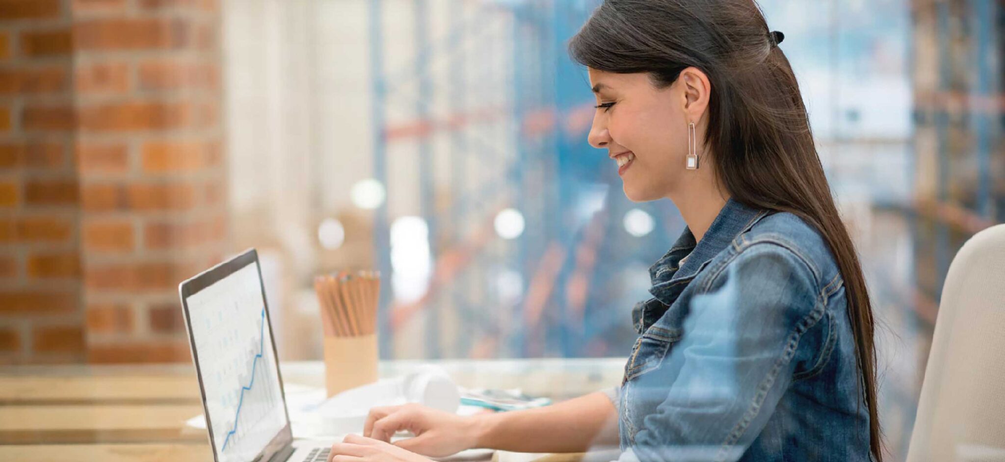 Woman working on a laptop in an office, smiling as she types.