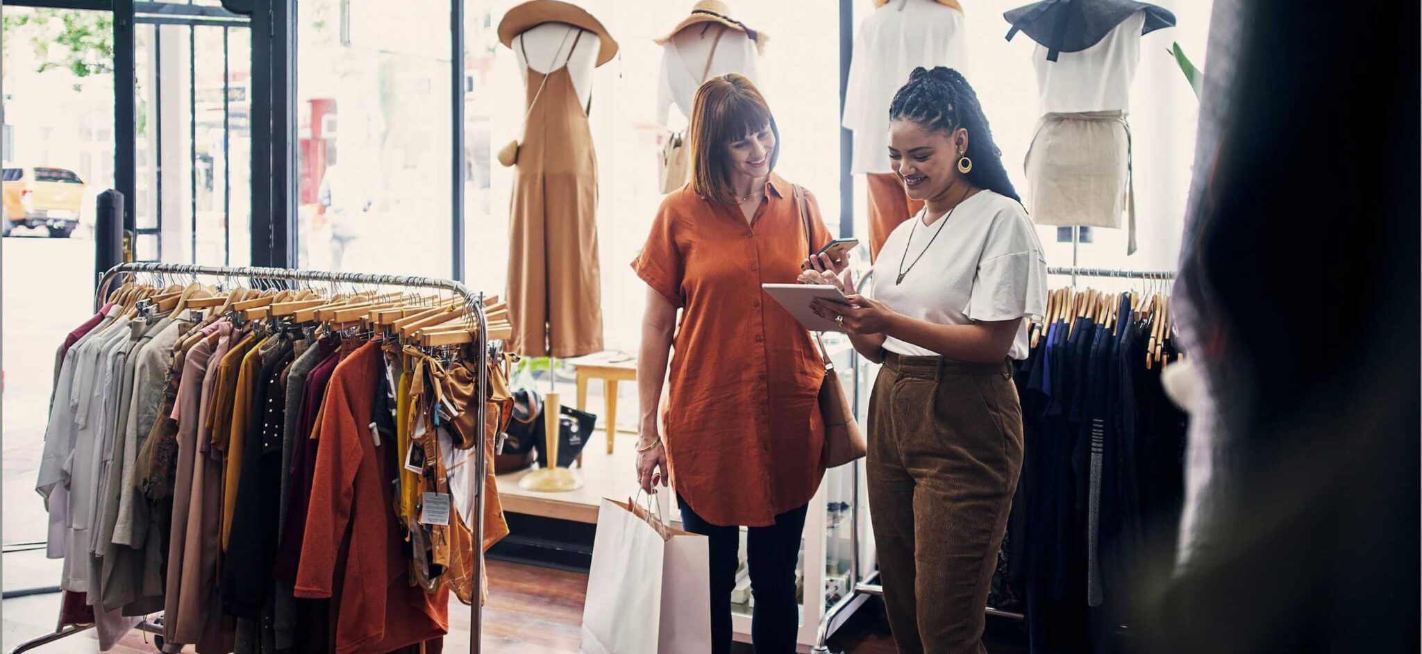 Two women discussing items in a clothing store, one holding a tablet.